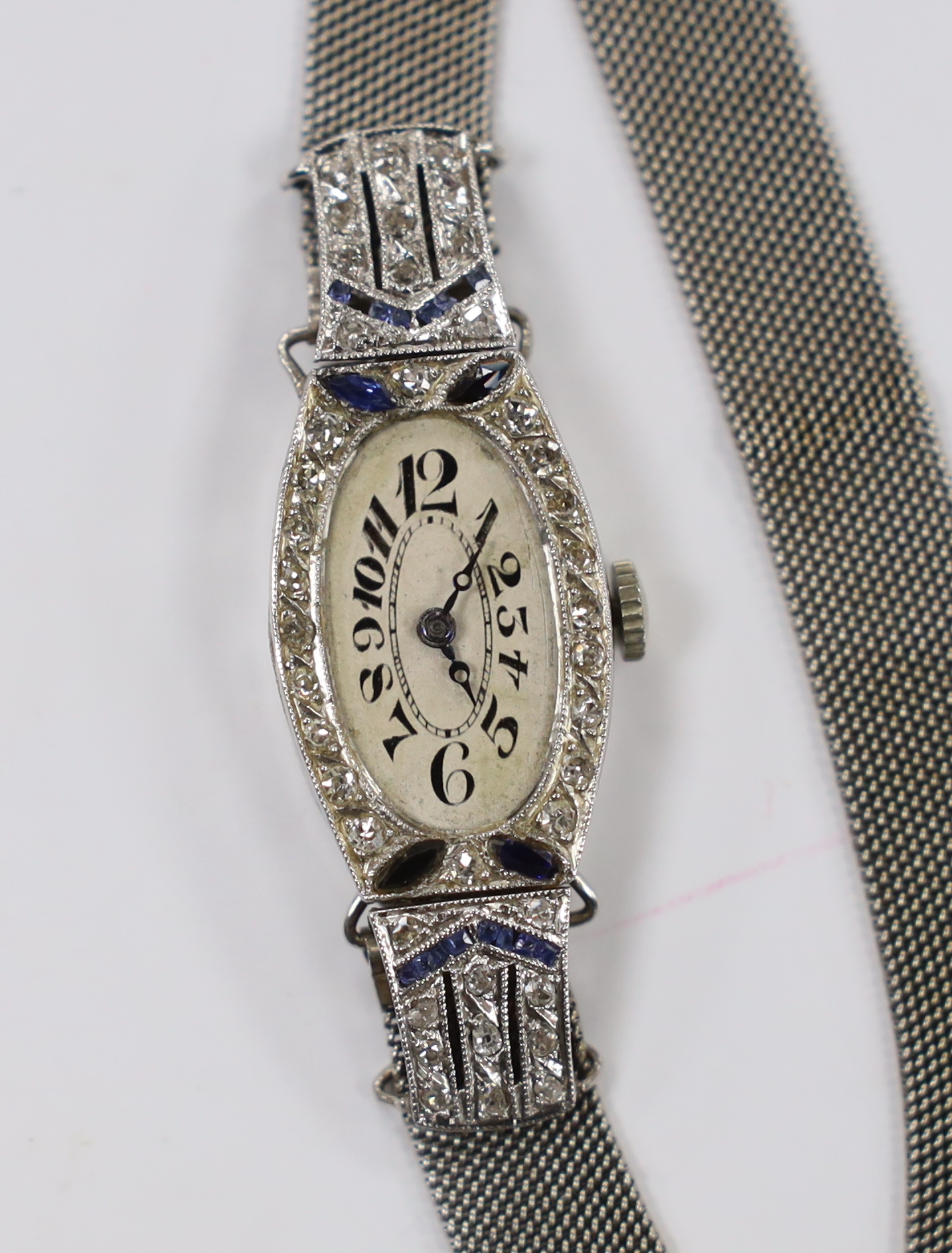 A mid 20th century white metal, sapphire and diamond cluster set Invicta Manufacturing Co. manual wind cocktail watch, on an adjustable 18ct white metal mesh bracelet, with oval Roman dial